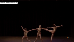 Three dancers on stage connected by holding hands